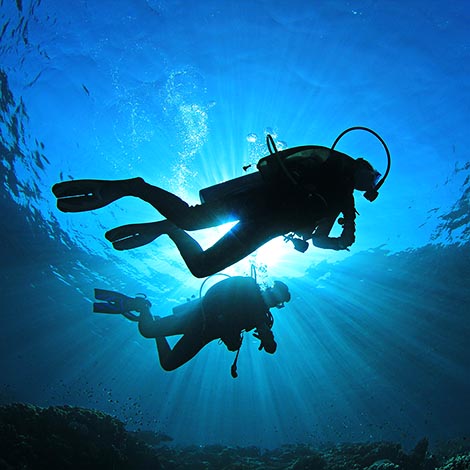 Two people scuba diving with sunlight from above Two scuba divers silhouetted against the sun while they explore a coral reef
