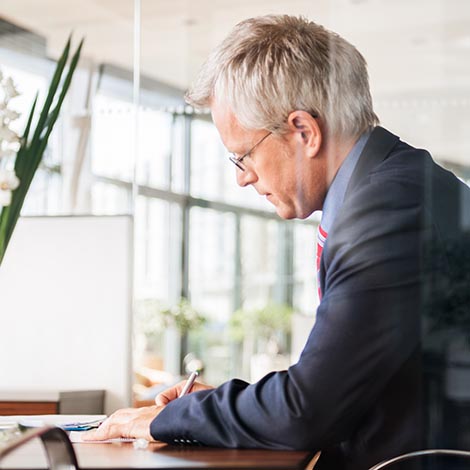 Mature businessman signing a paper or contract on a desk. Side view.