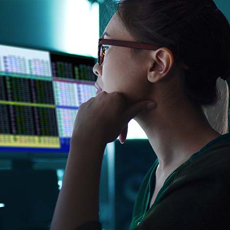 Stock photo of an Asian woman surrounded by computer monitors in a dark room