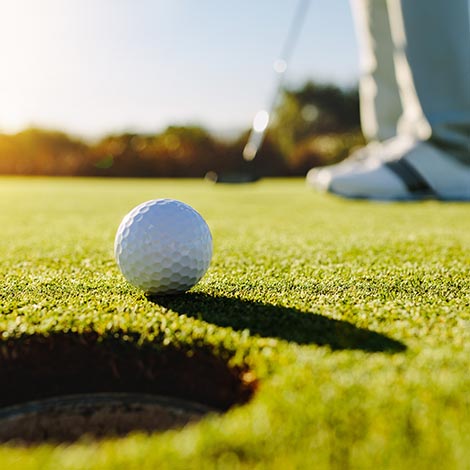 Professional golfer putting ball into the hole. Golf ball by the edge of hole with player in background on a sunny day.