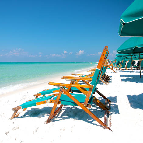 Sunny Adirondak beach chairs with umbrellas in the sand and surf