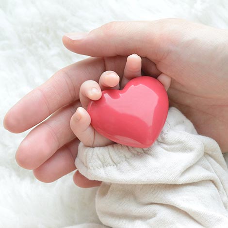 Baby's hand with heart object and mother's hand