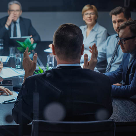 Late at Night In the Corporate Office Meeting Room: At Conference Table Executive Director Talks to a Board of Directors, Investors and Business Associates. Over the Shoulder Shot.