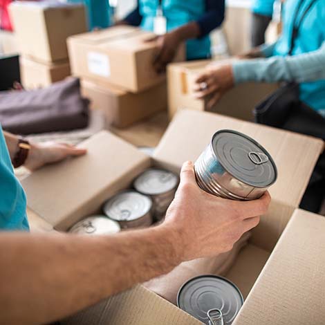 Man working at charitable foundation, packing cardboard donation box with canned food and blanket