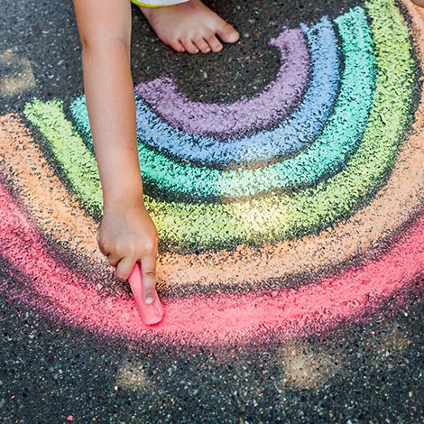the child girl draws a rainbow with colored chalk on the asphalt. Child drawings paintings concept. Education and arts, be creative when back to school