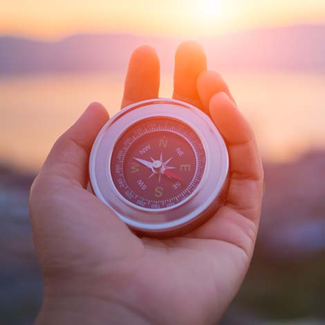 Closeup hand holding compass with  mountain and sunset sky background.