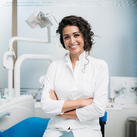 Portrait of a Caucasian woman dentist, sitting in her office next to a dentist chair, smiling