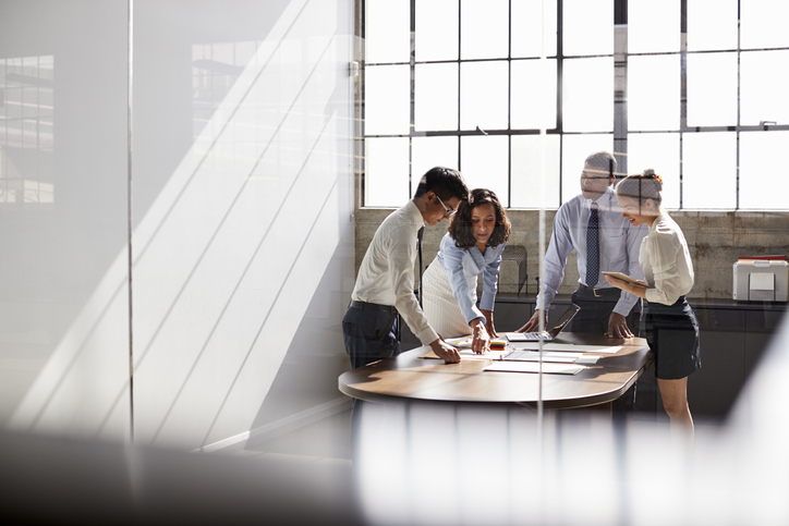 Four business colleagues stand talking in a meeting room Four business colleagues stand talking in a meeting room