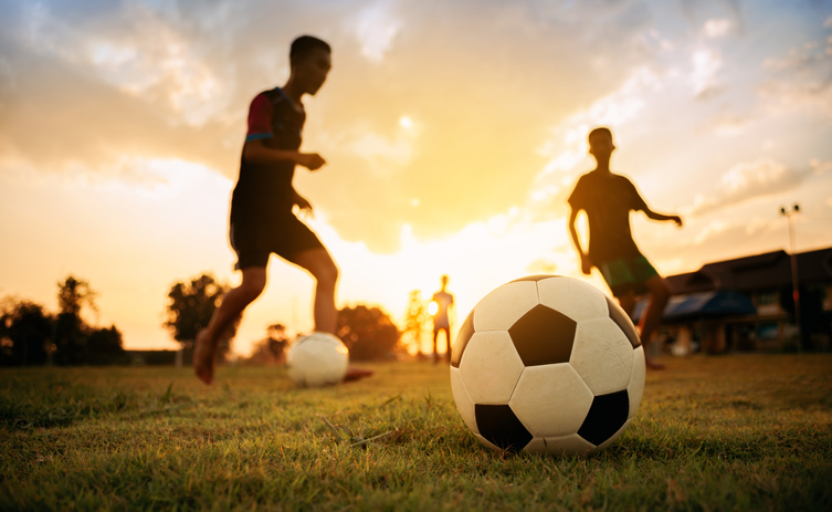 action sport outdoors of a group of kids having fun playing soccer football on the dirt field.