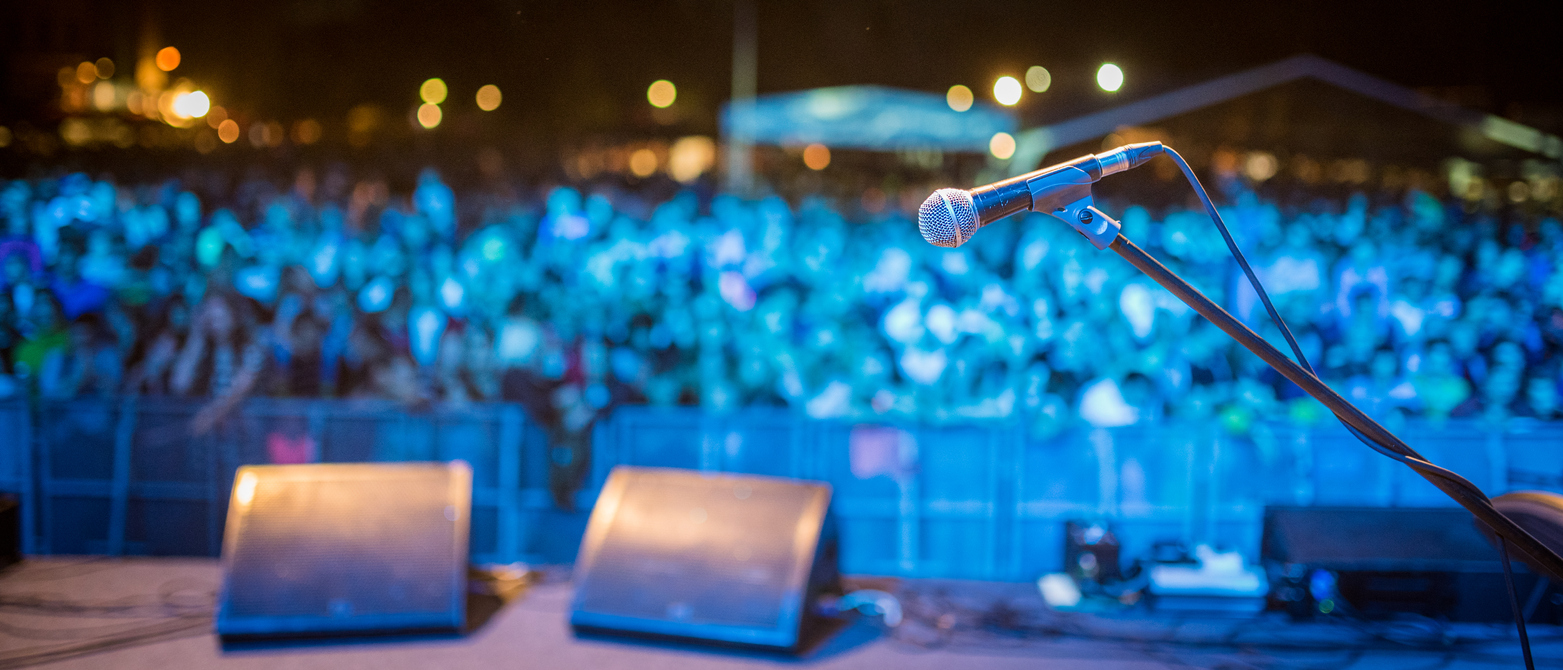 People standing before podium on open-air music festival and waiting for gig. Focused on microphone. Blue light on audience.