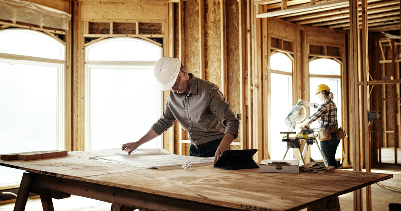 Architect looking over blueprints at home construction site.