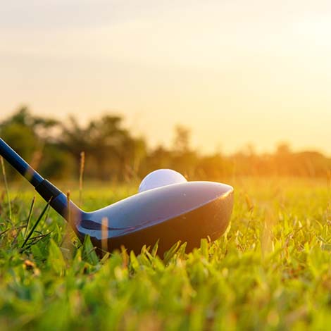 Close up golf ball and driver, player doing golf swing tee off on the green sunset evening time, presumably does exercise.  Healthy and Lifestyle Concept.