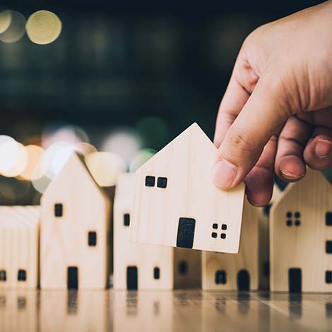 Hand choosing mini wood house model from model and row of coin money on wood table, selective focus, Planning to buy property. Choose what's the best. A symbol for construction ,ecology, loan concepts