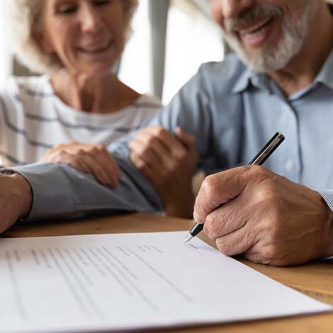 Close up of 60s husband and wife sit at desk sign health insurance contract close deal, smiling old mature couple spouses put signature on document make good agreement, elderly healthcare concept