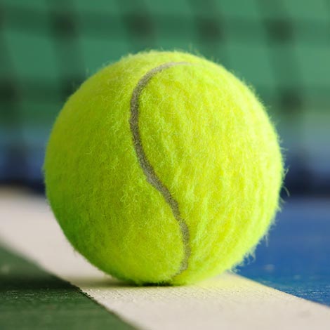 Tennis ball on the line with net in background in indoor tennis court