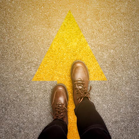 Feet and arrows on road background in starting line beginning idea. Top view. Woman in leather ankle boots on pathway with yellow direction arrow symbol. Moving forward, new start and success concept. Feet and arrows on road background in starting line beginning idea. Top view. Woman in leather ankle boots on pathway with yellow direction arrow symbol. Moving forward, new start and success concept.