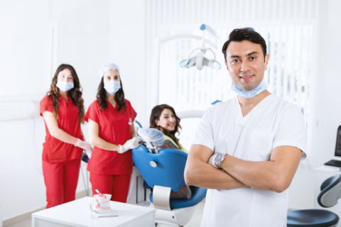 Dental team - one male dentist in white and 2 assistance in red next to a smiling patient in a blue chair