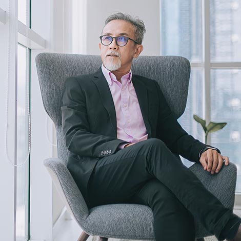 Successful Asian chinese senior businessman in suit sitting crossed leg on sofa in his office room looking at the capital city Successful Asian chinese senior businessman in suit sitting on sofa in his office room looking at the capital city
