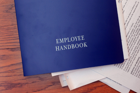 blue notebook on a wooden table reading employee handbook