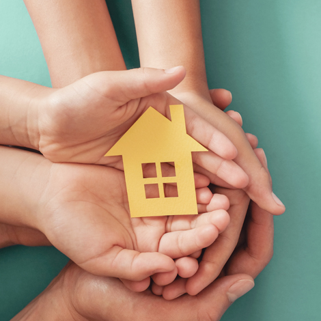 Hands holding yellow paper house on blue background