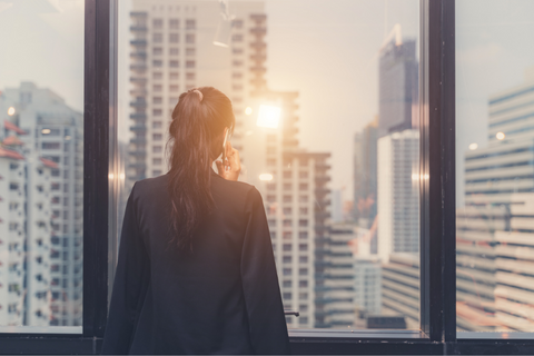 woman looking out a high-rise window at the sunset