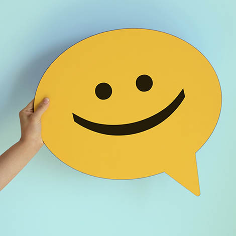 Women holding yellow speech bubble with smiley face cutout paper of a smiley chat face