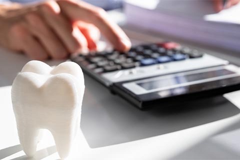 model of tooth and a male hand entering computation on desk calculator