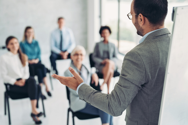 One person leading a discussion with five seated people as the audience