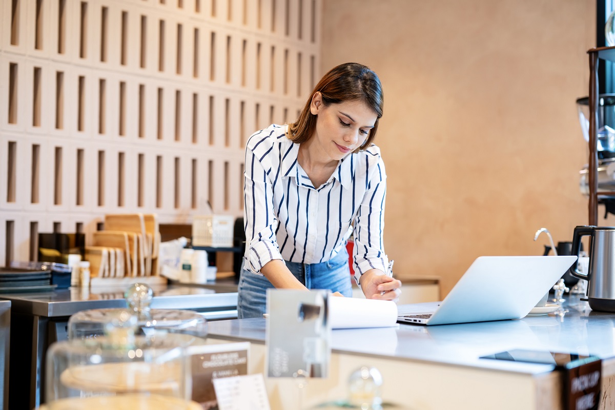 Coffee Shop and Restaurants Rewards Program Strategy Can Be a Fulfilling Demanding Experience. A female coffee shop owner uses a laptop computer to do business and marketing strategies to increase customers and sales in her coffee shop. - stock photo