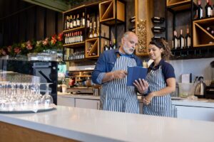 Happy business owner training a new employee at a coffee shop using a digital tablet - food service concepts