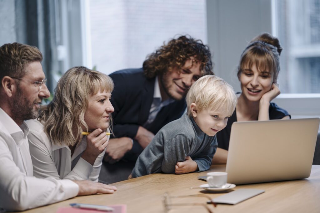 Multigenerational family gathered around a laptop, illustrating family office services of Aprio for wealth planning