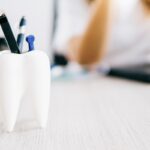 Tooth shaped pencil holder on desk - dentist with laptop on background