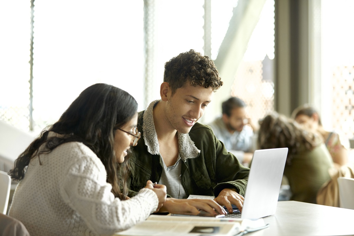 Smiling students studying over laptop in cafeteria