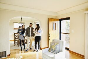 Wide shot for family with toddler in discussion with real estate agent while looking home for sale during open house