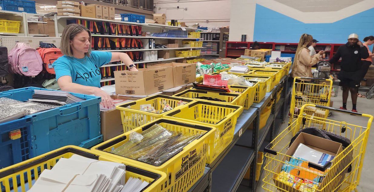 A woman in a blue Aprio tshirt sorts through donated school supplies