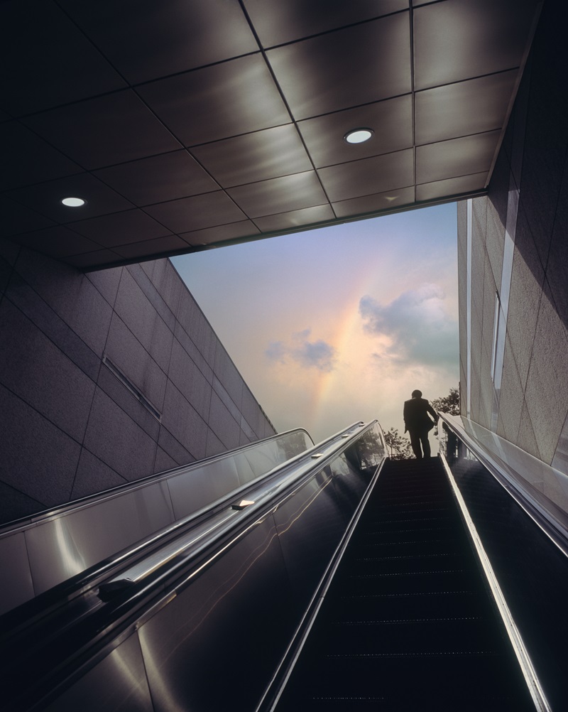 Businessman on escalator moving towards sky with rainbow