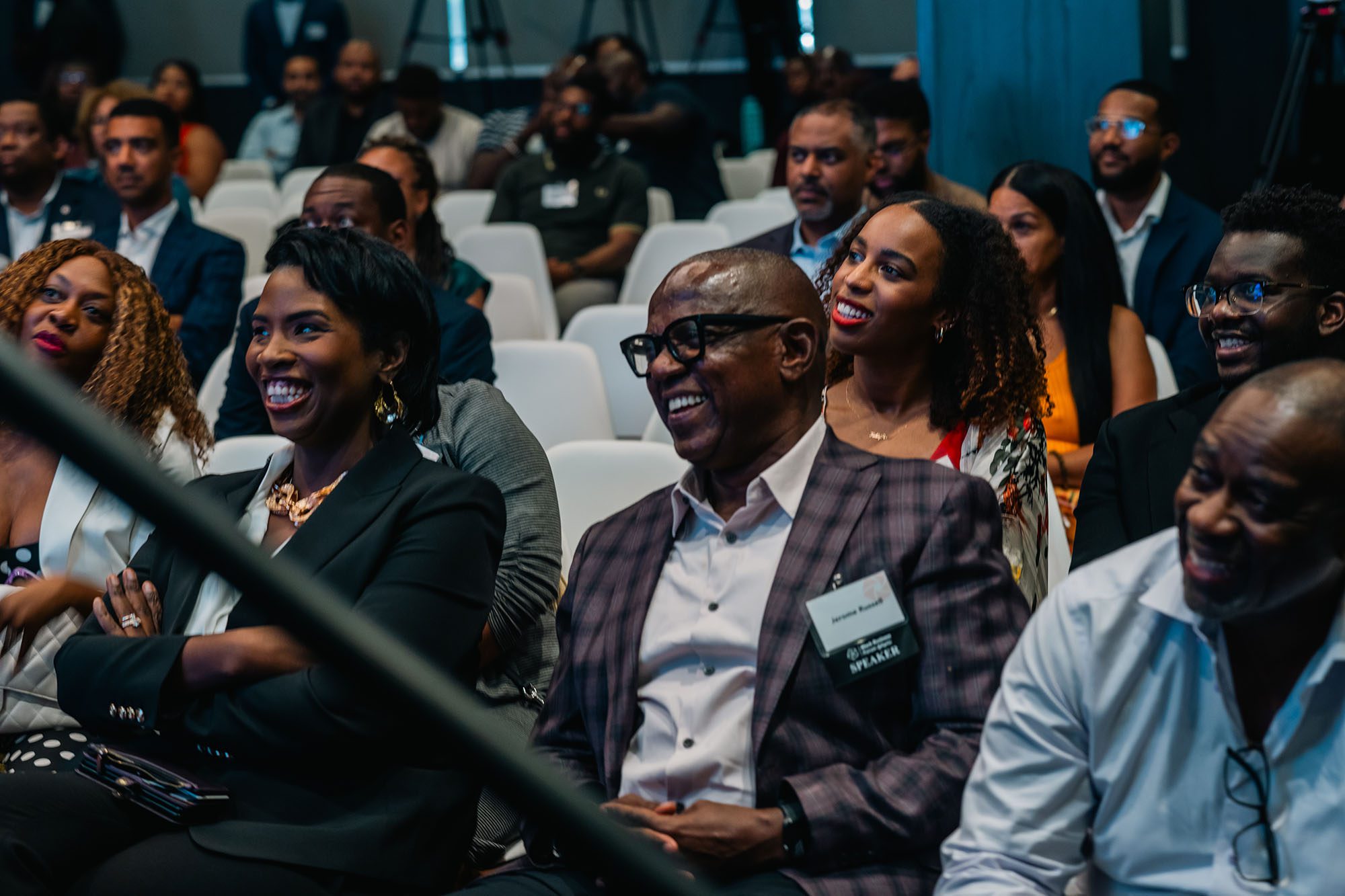 Close up of a crowd of well dressed attendees laughing at something off camera in a dark event space