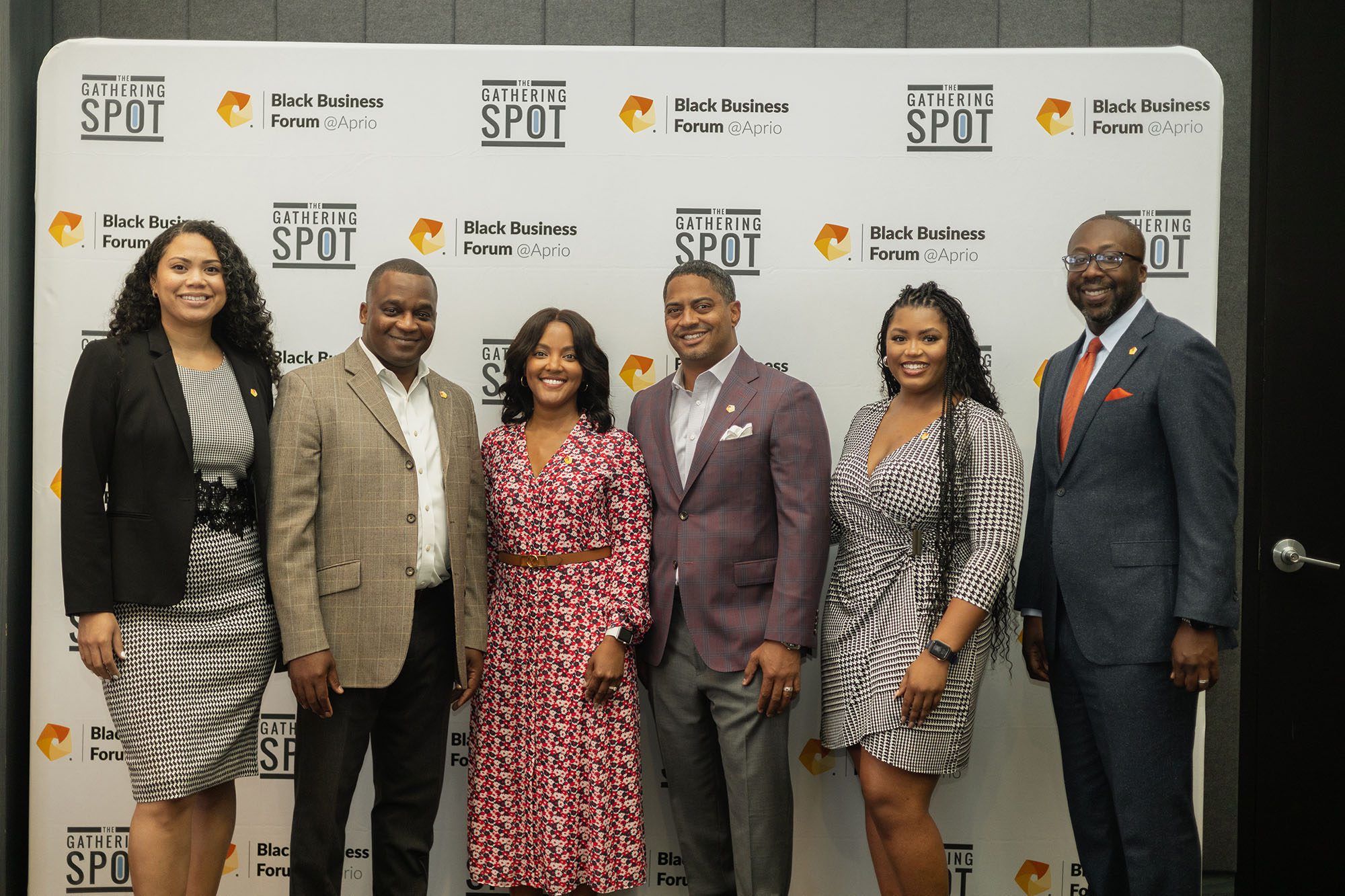 Four men and three women in business clothes pose in front of a white backdrop patterned with the Black Business Forum and Aprio logo