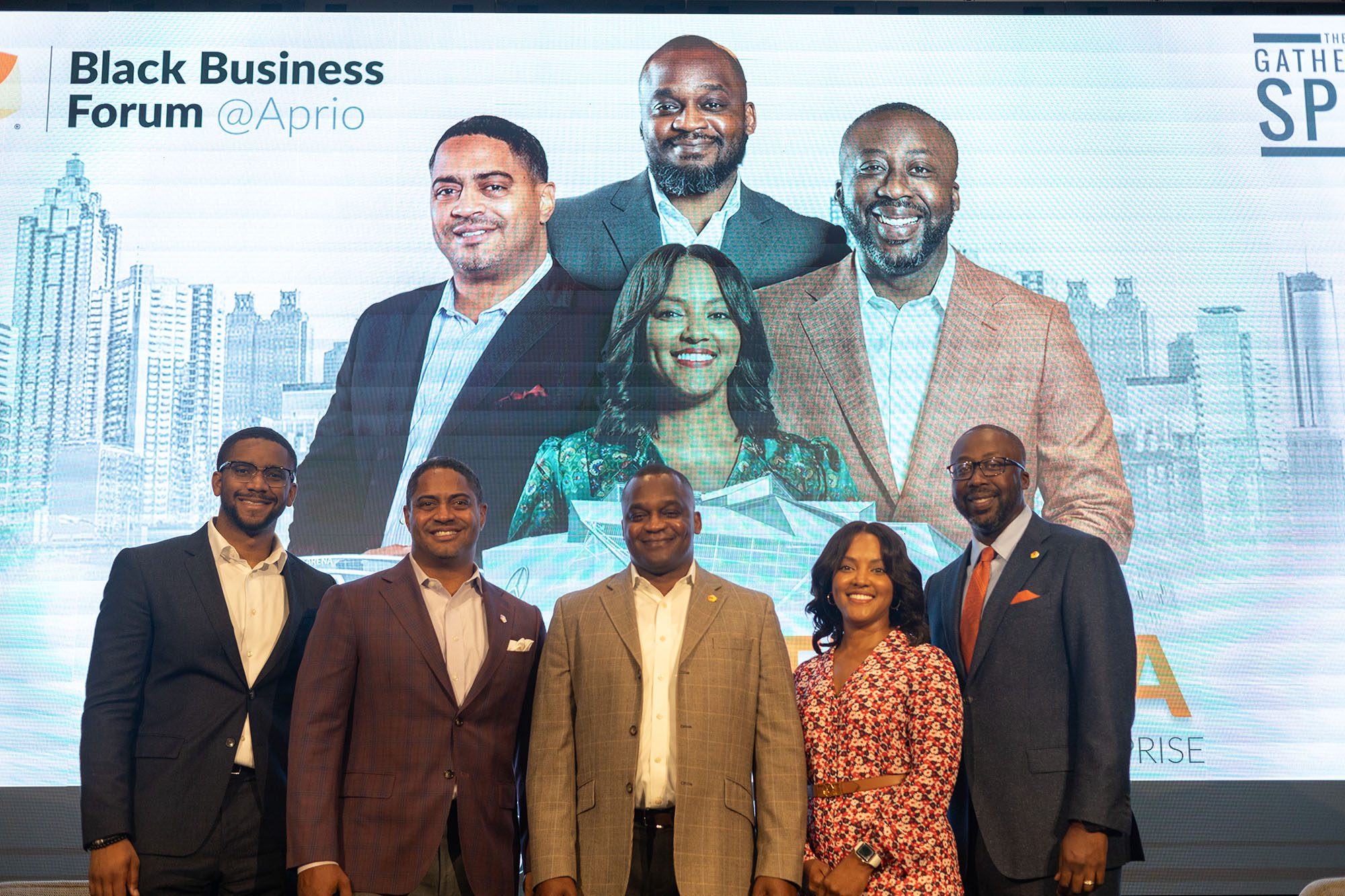 Four men and a woman smile together in front of a projection screen with their faces and 