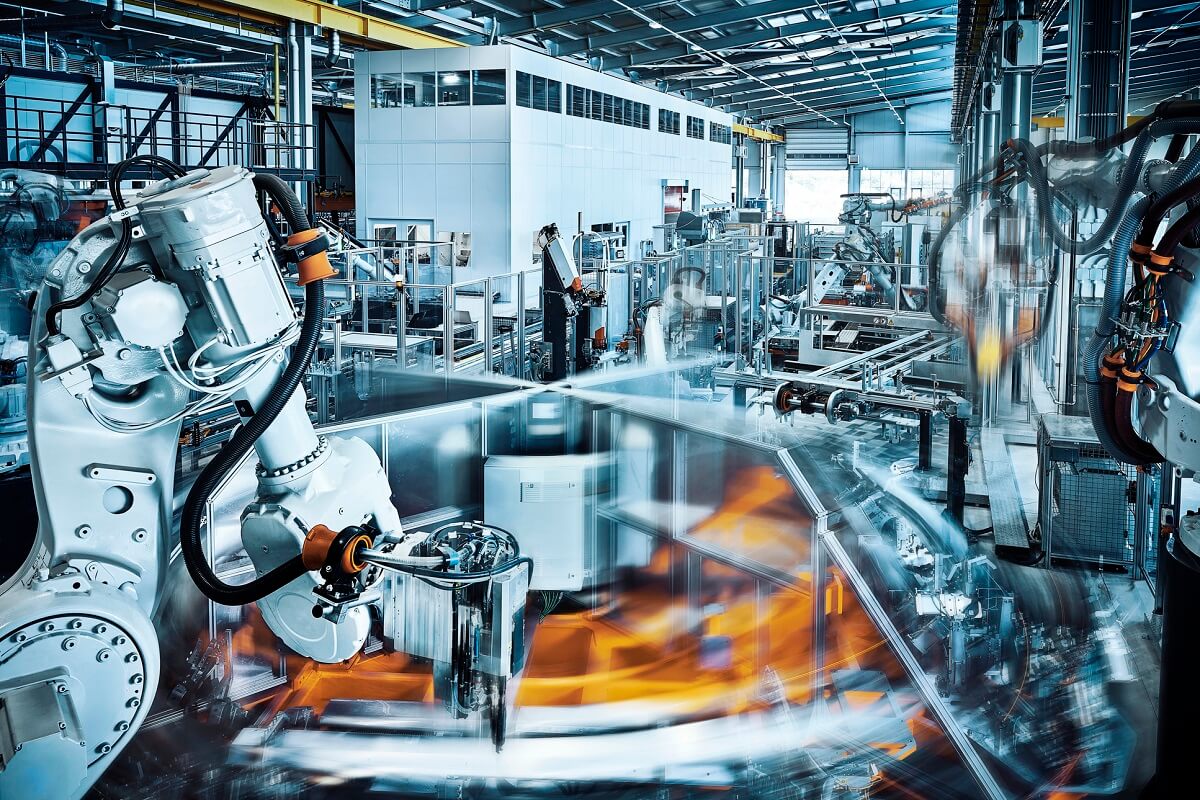 A robot arm in a robotics factory works alongside a blurred, fast-moving rotating wheel