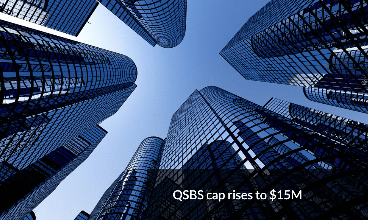 Shot from below, towering reflective skyscrapers soar up into a clear blue sky. Text in the bottom right reads 