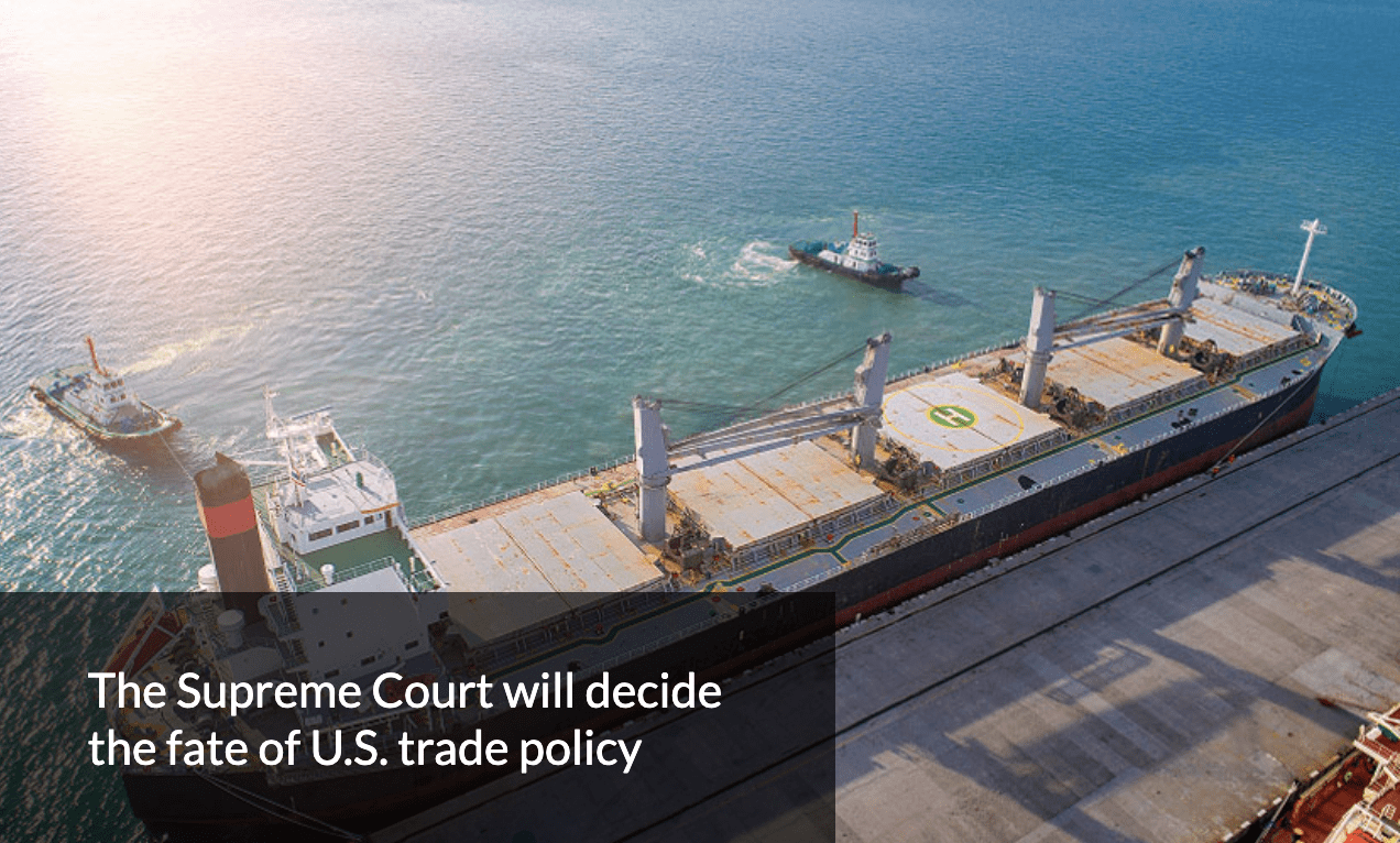 Aerial shot of a cargo ship alongside a light wooden dock in a blue sea. Text in bottom left reads 