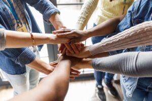 Close up shot of unrecognizable group of diverse individuals forming a united front, holding their hands stacked in a gesture of solidarity.