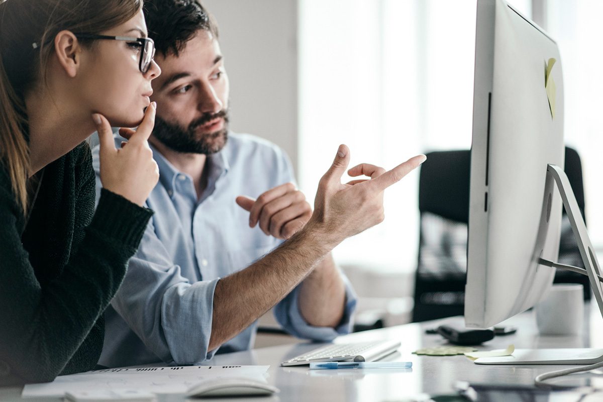 Man and woman sitting at a desk and looking at a computer monitor in a bright space