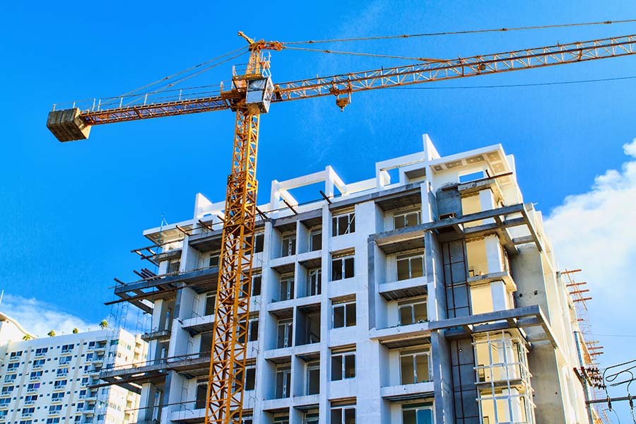 A yellow tower crane stands next to a multi-story building under construction against a blue sky.