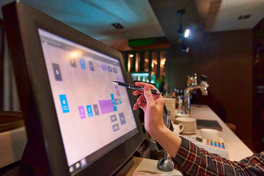 A person uses a pen to select options on a touchscreen point-of-sale system at a bar or restaurant counter.