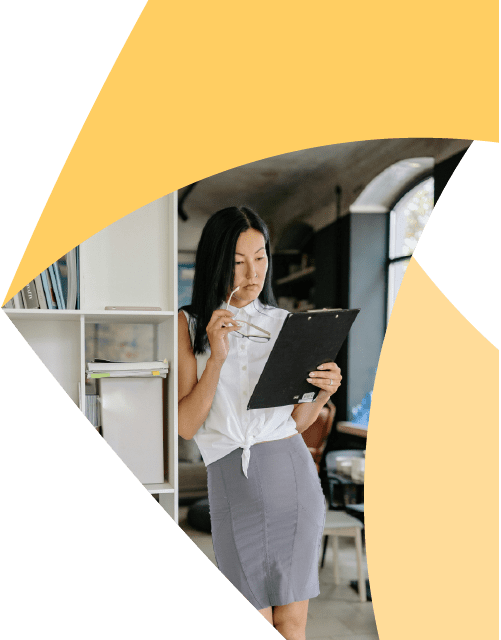 In a corner of the Aprio pinwheel logo, a businesswoman leans against a shelf in an office and looks at a clipboard