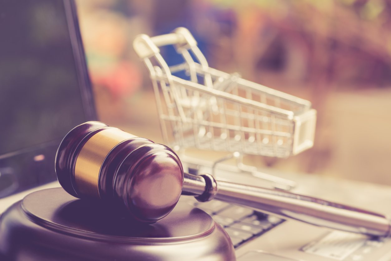 A judge’s gavel rests on a laptop keyboard next to a small metal shopping cart, symbolizing online shopping and internet law.