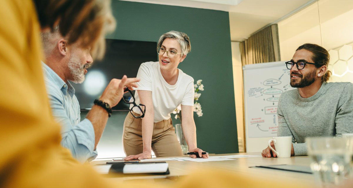 Group of men and women sitting in a green-walled conference room and having a lively discussion