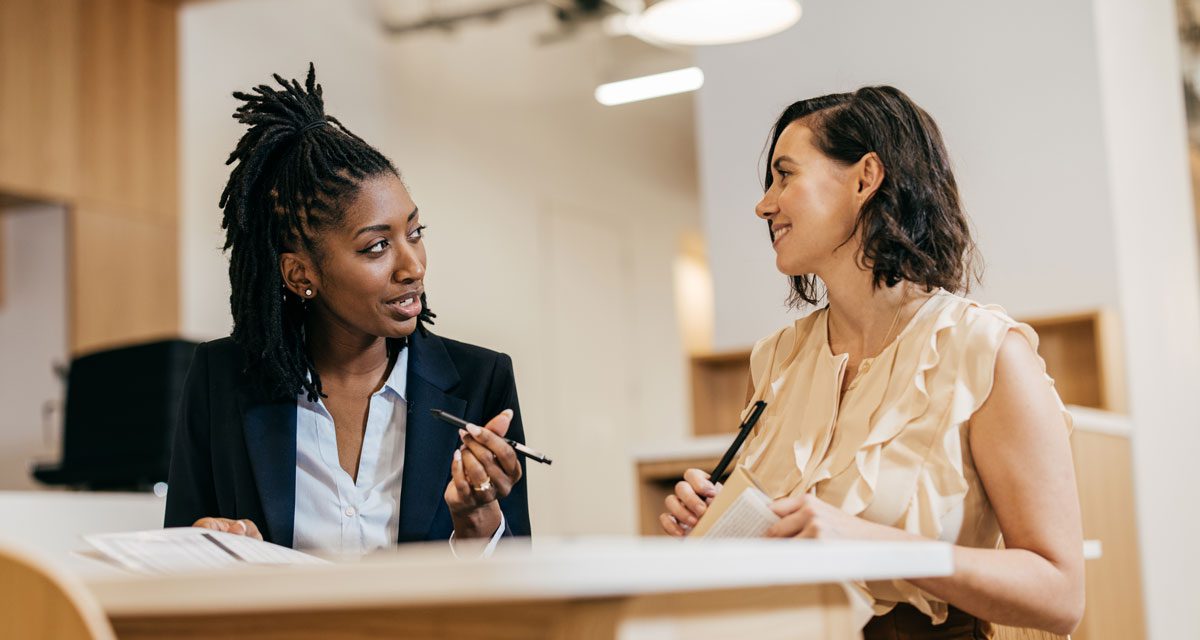 Two women conversing at a table in an office setting